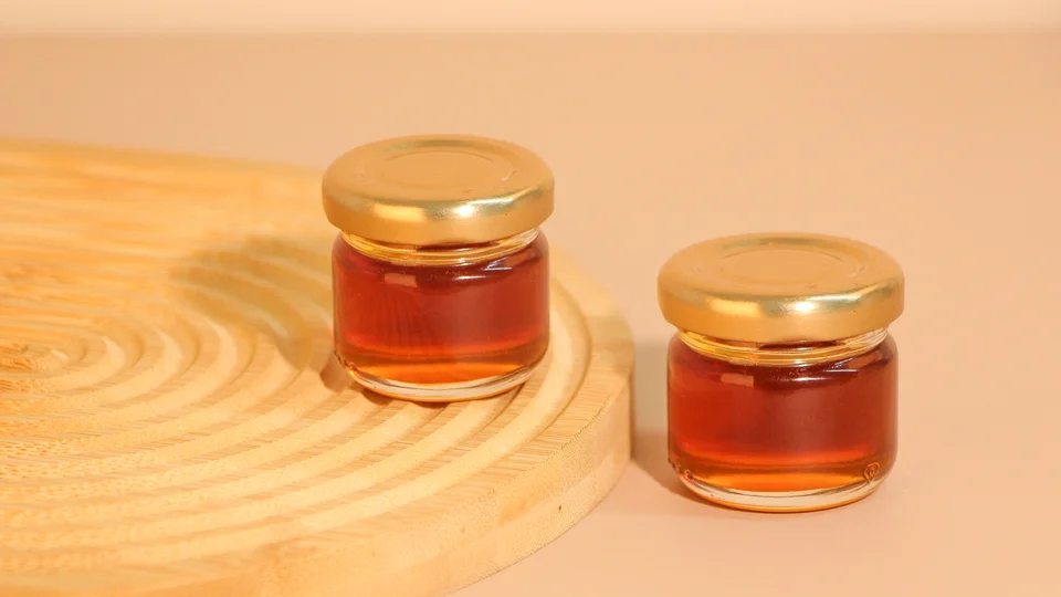 Small glass honey jars with gold lids on a wooden display
